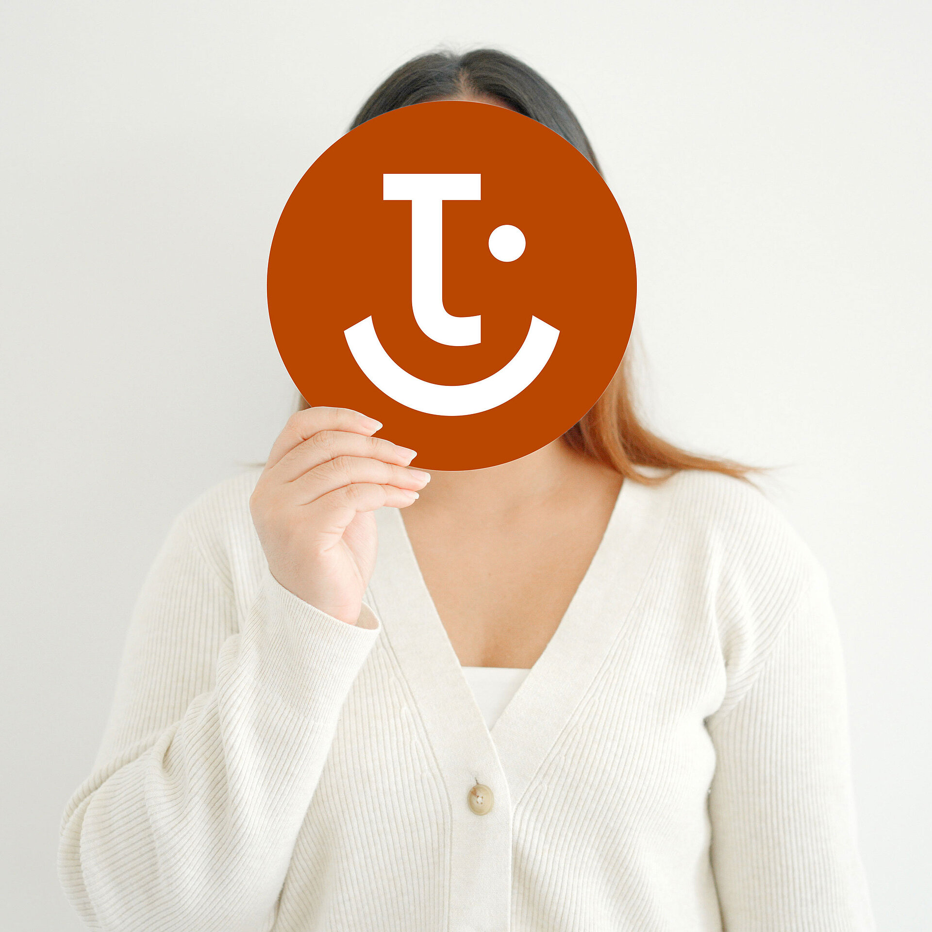 Frau hält rundes Schild mit lächelndem Logo vor das Gesicht